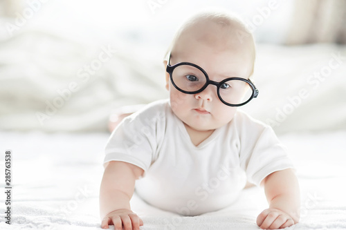 A newborn baby is lying on a soft bed in glasses.