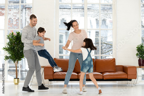 Happy parents and children laughing dancing together in living room