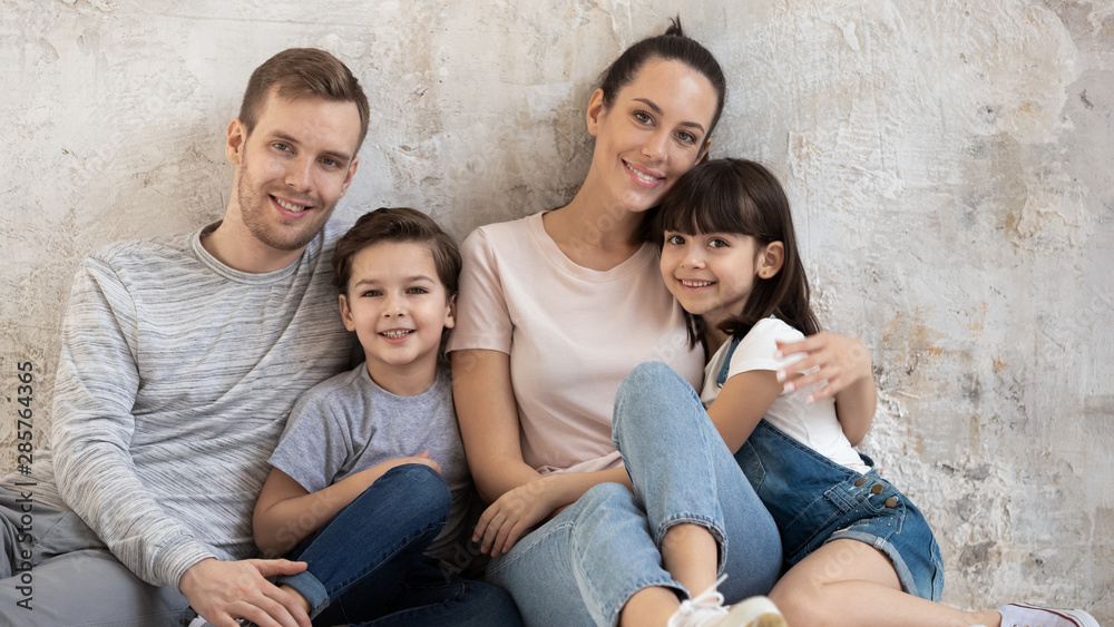 Happy family sit on floor in apartment looking at camera