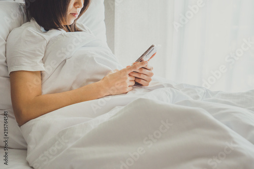 Asian Girl in bed room on the bed with the mobile phone.Closeup portrait of young sleepy exhausted woman lying in bed using smartphone,