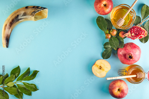 Rosh hashanah - jewish New Year holiday concept. Traditional symbols: Honey jar and fresh apples with pomegranate and shofar -horn on a blue background. Copy space for text. photo