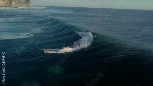 Man on a jet ski helps his surfer friend pick up speed from a big wave