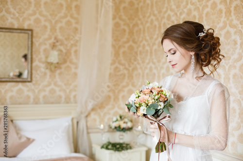 Pretty young Bride.Brown-haired woman with classic wedding hair-style. Boudoir morning of the bride. Taking wedding bouquet in her hands