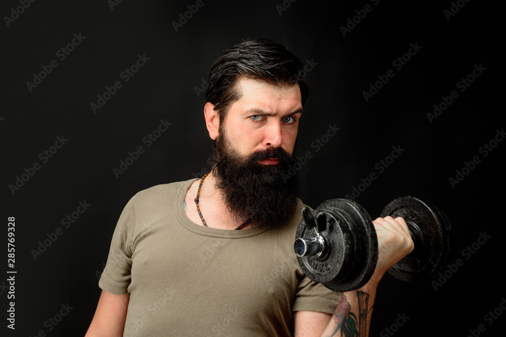 Handsome man lifting dumbbell at gym. Athletic young male fitness model holds dumbbell. Fit young man in sportswear holds dumbbell during workout in gym. Healthy sports lifestyle, fitness concept.