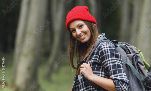 Cheerful brunette tourist girl wearsing cap and backpack having walk through the forest, tourism concept