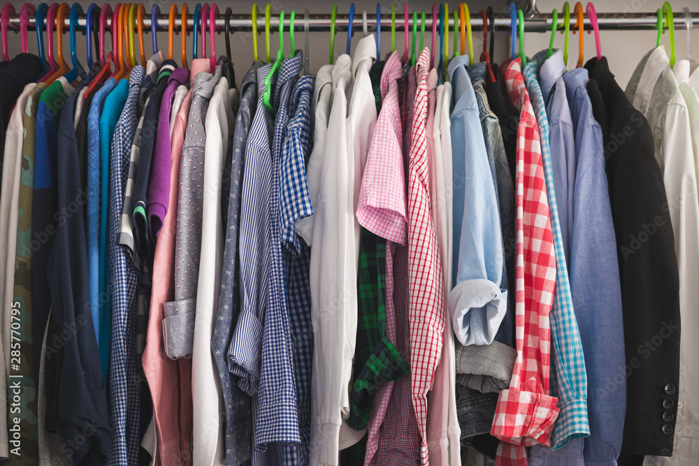 Close-up of hangers with different fashionable clothes. Children's clothes of different colors are hung on hangers in the wardrobe room. Shirts, T-shirts and other children's clothing Close-up of hangers with different fashionable clothes. Children's clothes of different colors are hung on hangers in the wardrobe room. Shirts, T-shirts and other children's clothing