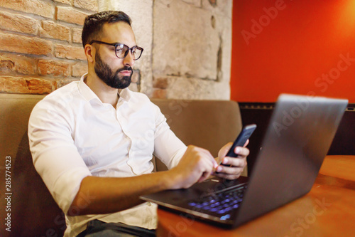 Smart bearded man working with laptop during drinking coffee in working space