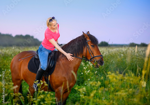 One Caucasian woman is astride her bay horse on a pasture in outdoors.