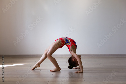 Small girl rhythmic gymnast is doing over-turn exercise on the light background