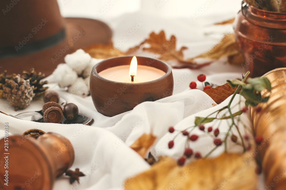 Autumn mood. Candle, berries, fall leaves, herbs, acorns, nuts and brown hat on white fabric. Hello autumn, cozy inspirational image. Hygge lifestyle