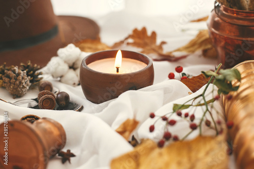 Autumn mood. Candle, berries, fall leaves, herbs, acorns, nuts and brown hat on white fabric. Hello autumn, cozy inspirational image. Hygge lifestyle