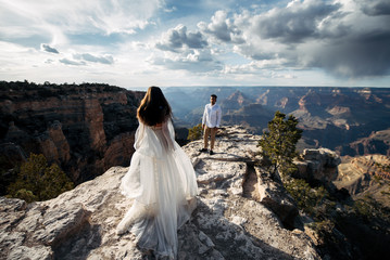 The bride goes to the groom on the rocks, the dress flutters in the wind