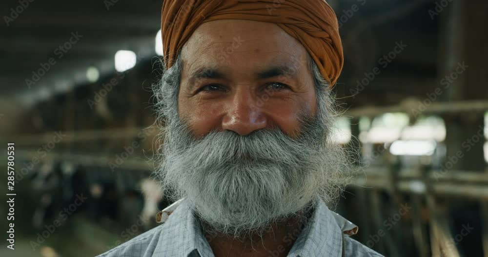 Cinematic portrait of senior indian worker is smiling in camera satisfied with his work on a background of dairy farm.