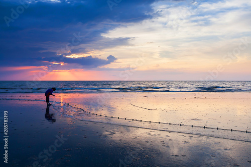 Asian woman catching saltwater fish on the beach at dusk.