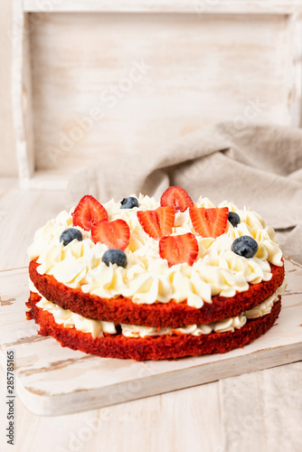 Red velvet cake with white cream and fruit and berries decoration on wooden table