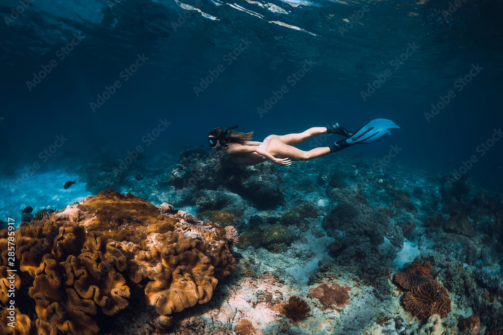 Freediver woman with fins glides over coral bottom in underwater