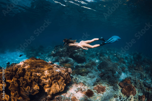 Freediver woman with fins glides over coral bottom in underwater