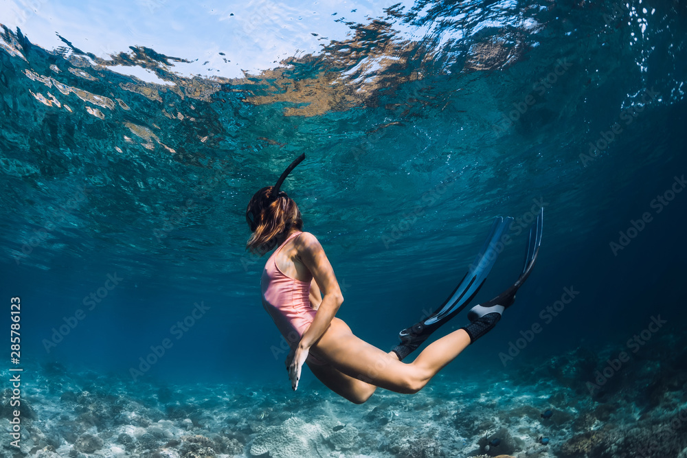 Woman freediver swim in pink swimsuit underwater with fins. Freediving underwater in ocean