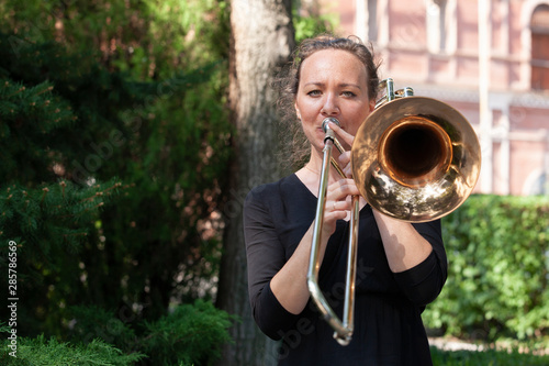 Girl learning to play trombone. Portrait of a girl on a background of a city park park.