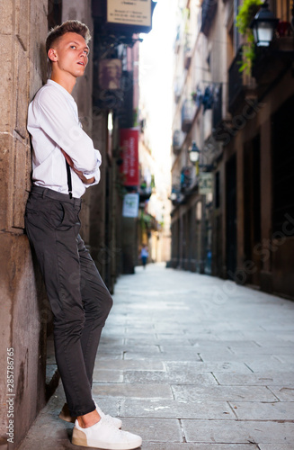 young European guy in shirt and trousers with suspenders walking around city © caftor