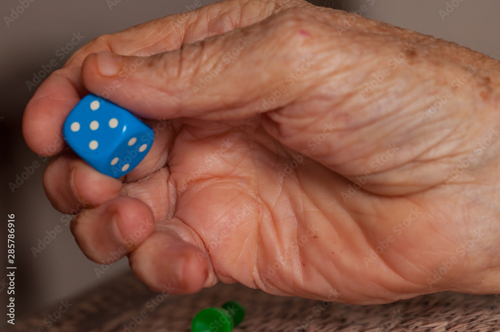 Grandma rolls a blue dice.Social game. Throwing a blue cube Grandma rolls a blue dice.Social game. Throwing a blue cube
