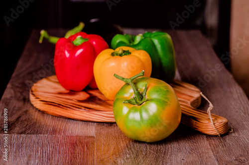 Pimientos verdes  rojos y amarillos sobre tabla de cortar junto a tomate verde y berenjena