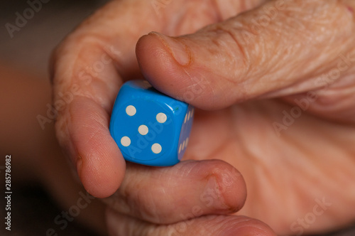 Grandma rolls a blue dice.Social game. Throwing a blue cube