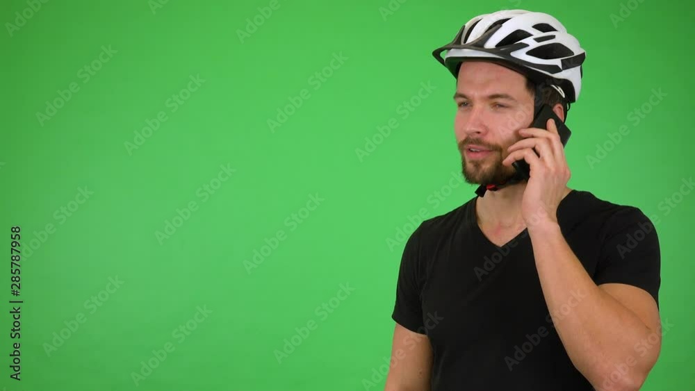A young handsome cyclist talks on a smartphone, then smiles at the camera - green screen studio A young handsome cyclist talks on a smartphone, then smiles at the camera - green screen studio