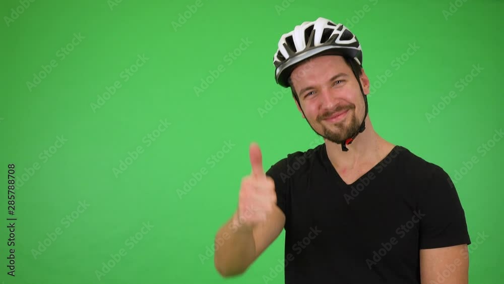 A young handsome cyclist shows a thumb up to the camera with a smile - green screen studio A young handsome cyclist shows a thumb up to the camera with a smile - green screen studio