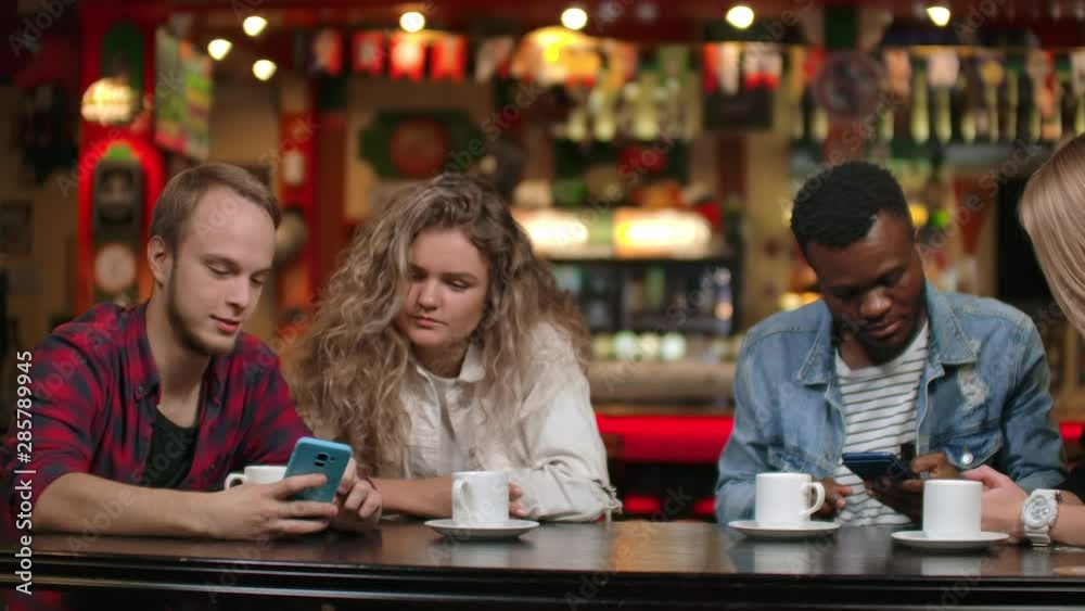 Two men and Two women multi-ethnic couples sit in a cafe and look at the screens of smartphones and discuss Two men and Two women multi-ethnic couples sit in a cafe and look at the screens of smartphones and discuss