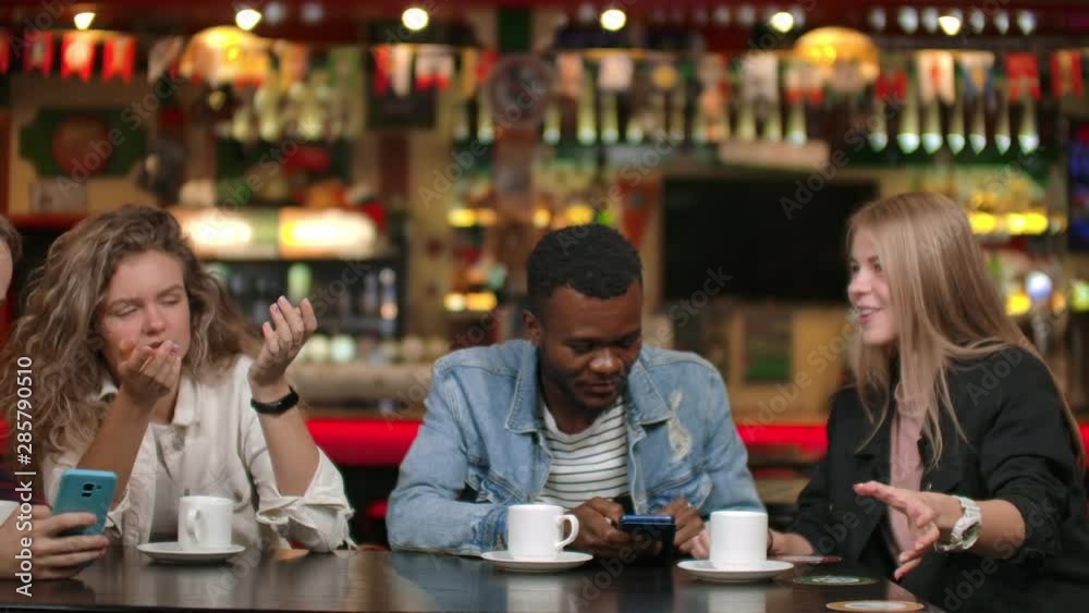 Happy diverse mates having fun with gadget together watching funny online video on smartphone, multicultural young friends laughing looking at phone talking use mobile apps at meeting sit at table. Happy diverse mates having fun with gadget together watching funny online video on smartphone, multicultural young friends laughing looking at phone talking use mobile apps at meeting sit at table.