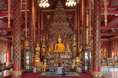 nside a Buddhist temple in Thailand, chaired by a large golden Buddha, in the middle there is a tourist on her knees who takes pictures © Albert