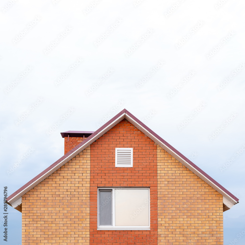 Part of a red brick private building against a clear sky. Triangular roof and a window on the house. Copy space for articles on new affordable housing under the state program or mortgage lending. Part of a red brick private building against a clear sky. Triangular roof and a window on the house. Copy space for articles on new affordable housing under the state program or mortgage lending.