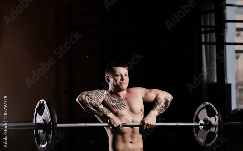 Young handsome guy with a naked torso doing exercises in the gym