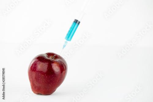 Concept: human GMO manipulation of nature and relative poisoned fruits. Close-up of an apple contaminated with a syringe threaded in and white background