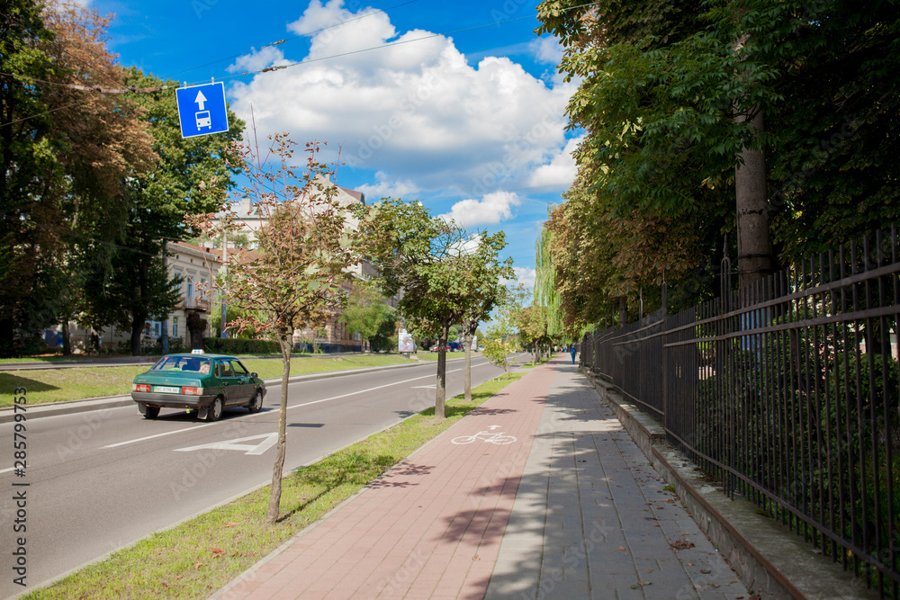 Fototapeta premium Protected bike lane between parking lane and sidewalk on city street. Bikers commuting on nice spring day.