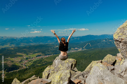 The girl at the top of the mountain raised her hands up. Wide summer mountain view at sunrise and distant mountain range covered. Beauty of nature concept