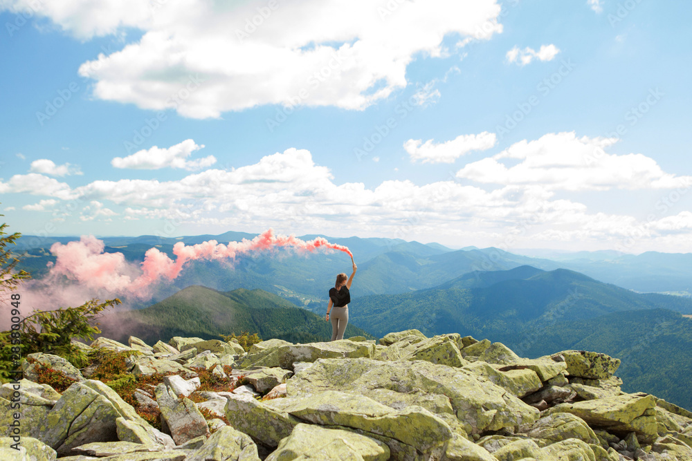 Beautiful woman with red colored smoke at the top of the mountain and cloudy sky background
