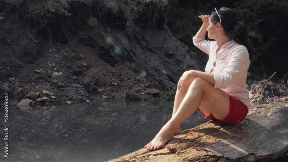 A beautiful girl sits on an log and admires nature. The girl enjoys nature and the sun. A beautiful girl sits on an log and admires nature. The girl enjoys nature and the sun.