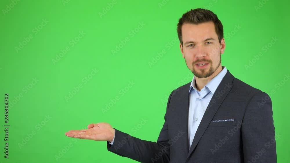 A young handsome businessman talks to the camera, puts out a hand with a product and continues talking - green screen studio A young handsome businessman talks to the camera, puts out a hand with a product and continues talking - green screen studio