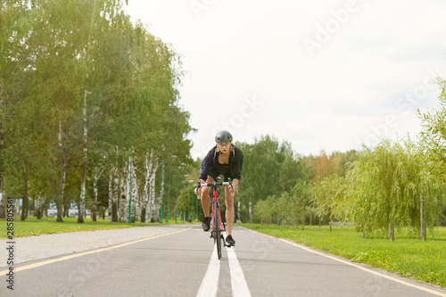 Fototapeta Naklejka Na Ścianę i Meble -  Sportswoman in uniform and helmet riding on the bike path on the background of green trees