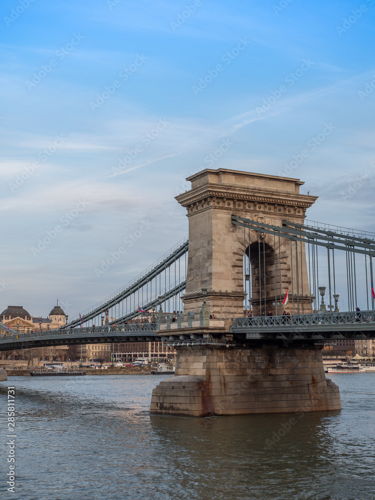 Obraz premium Budapest, Hungary - Mar 9th 2019: The Széchenyi Chain Bridge is a suspension bridge that spans the River Danube between Buda and Pest, the western and eastern sides of Budapest, the capital of Hungary