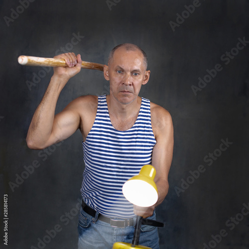 A man with a stick in one hand and a luminous yellow table lamp in the other hand.