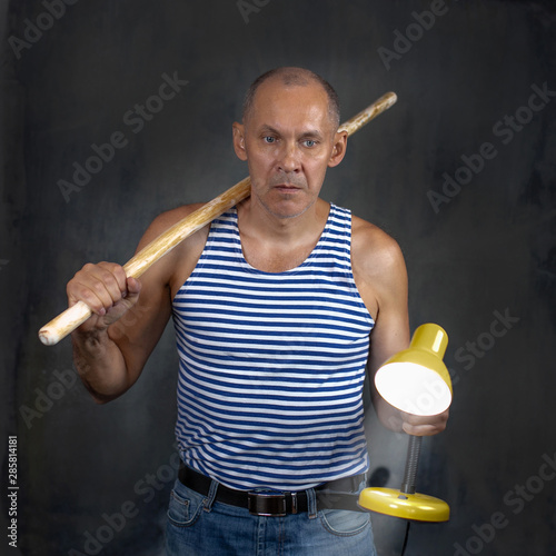 A man with a stick in one hand and a luminous yellow table lamp in the other hand.