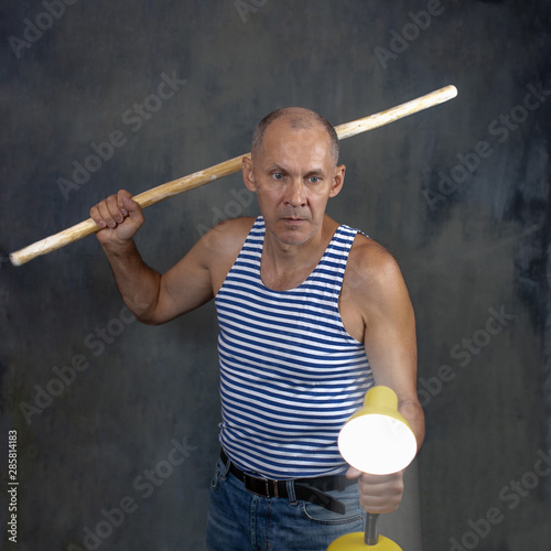 A man with a stick in one hand and a luminous yellow table lamp in the other hand.