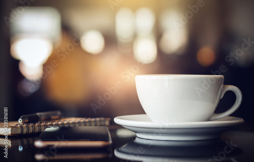 Zbliżenie biała filiżanka kawy z smartphone, notatnikiem i piórem na stole w kawiarni. Tło światło, niewyraźne i bokeh