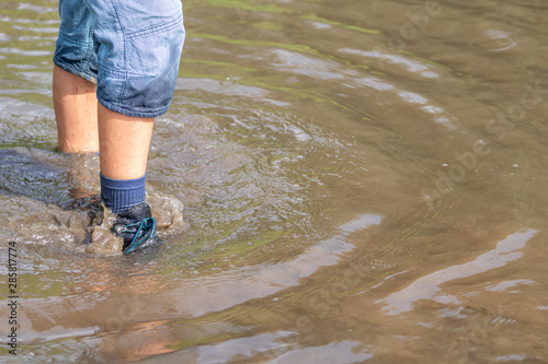 Junge watet mit nassen Schuhen und nassen Socken durch Hochwasser nach einer Überschwemmung mit starkem Regen und Deichbruch