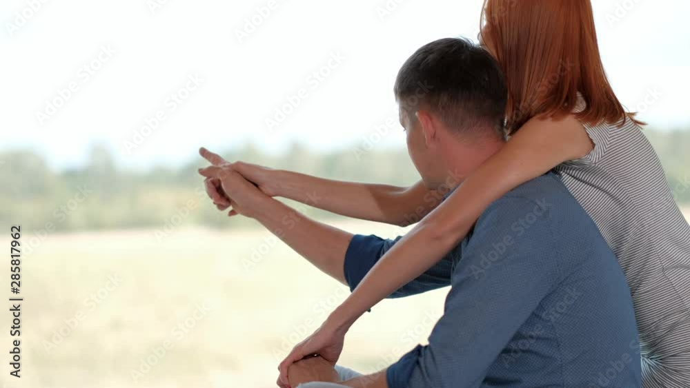 A couple, a man and a woman, Caucasians are lying and sitting on the bed near the large window of the village house. Hug, kiss and look out the window. Vacation concept of a couple in love at the week A couple, a man and a woman, Caucasians are lying and sitting on the bed near the large window of the village house. Hug, kiss and look out the window. Vacation concept of a couple in love at the week