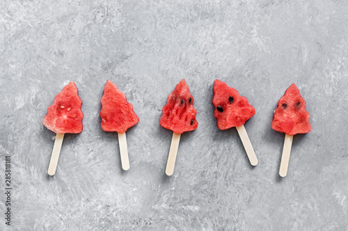 Popsicles on a stick of watermelon in the shape of a Christmas tree on a gray rustic background. Top view, flat lay.