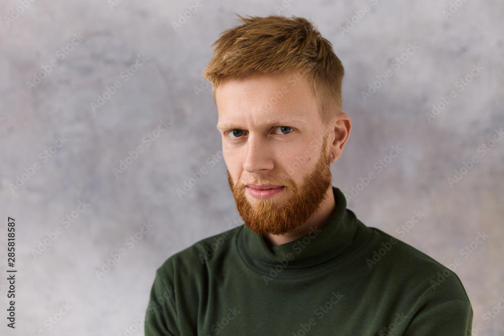 Isolated image of attractive red haired bearded young Caucasian male dressed in elegant stylish clothes staring at camera with intense concentrated look. Human facial expressions and attitude